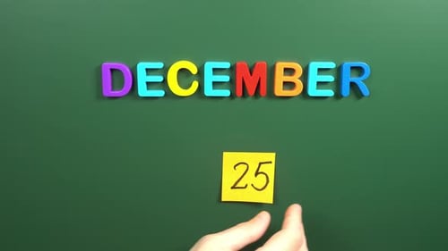 Hand sticking a sticker 25 December calendar day on school board. 25 date of December. Twenty fifth