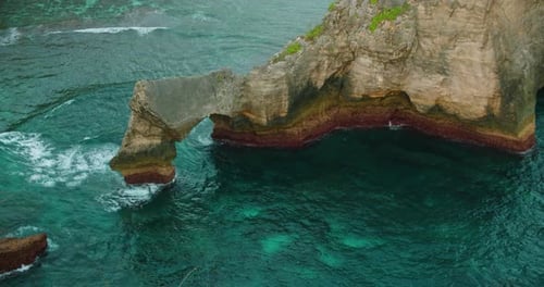 Natural rock arch formation in turquoise ocean water at Atuh Beach in Nusa Penida Indonesia
