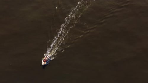 Isolated fishing motorboat leaves long white wake trail over brown and calm sea water. Aerial top do