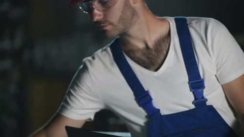 Hält Laptop. Ein Mann in Uniform arbeitet an der Produktion. Industrielle moderne Technologie