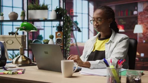 Woman in Home Office Stretches Back Feeling Fatigued While Working on Laptop