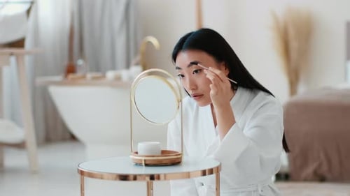Woman Applying Makeup in a Modern Bathroom Setting During Daytime