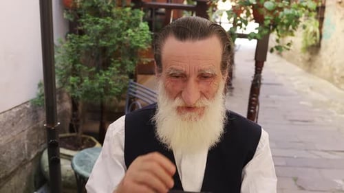 Elderly Man Using Smartphone at Outdoor Cafe