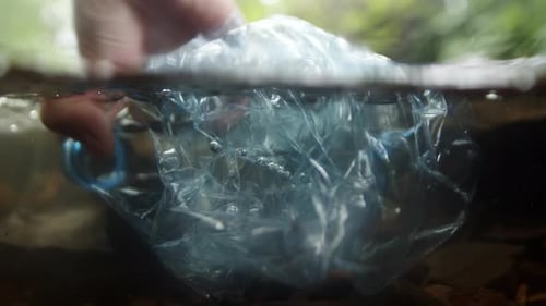 Öko-Freiwilliger sammelt Plastikmüll von Hand aus einem Waldbach in Unterwasseransicht