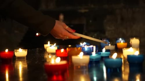 Shot of the hand of a young woman praying, lighting a candle in a Catholic Church.