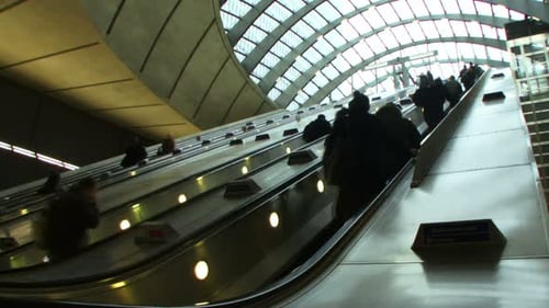 Low angle wide shot commuters on escalators under glass canopy at Canary Wharf station London