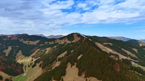 Mountains with wooded areas and bare grassy ones. Rocky background under the cloudy sky.