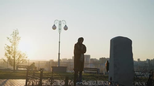 Tränenreiche Frau, die vor einem Steindenkmal bei Sonnenuntergang in einem Park nachdenkt