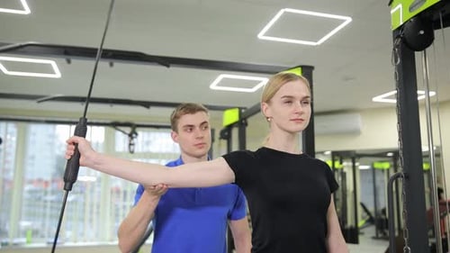 A Dedicated Fitness Trainer Helps a Woman Work Out in a Modern and Wellequipped Gym