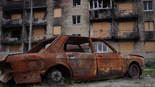 Side View Rusty Burnt Out Automobile on Street at Ashed Residential House Outdoors