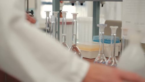 Eine Reihe transparenter flüssiger Flüssigkeiten im Labor. Eine Glasflasche wird von einem Kaukasier weggenommen