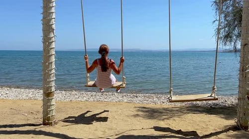 Redhead little girl on summer holiday enjoy swinging on rope swing looking at calm sea