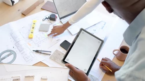 Using tablet and discussing blueprints, business colleagues collaborating in office