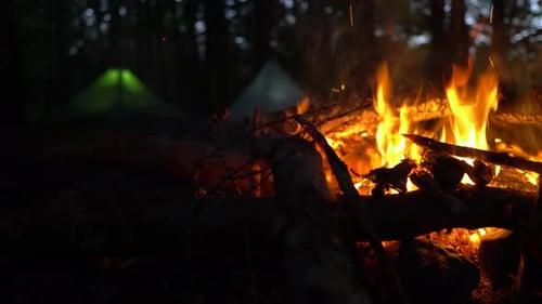 Revealing rack focus shot of campfire and two glowing tents at night in forest