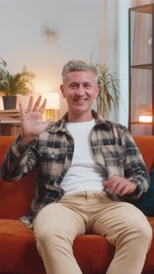 Man Waving Sitting on Couch Indoors