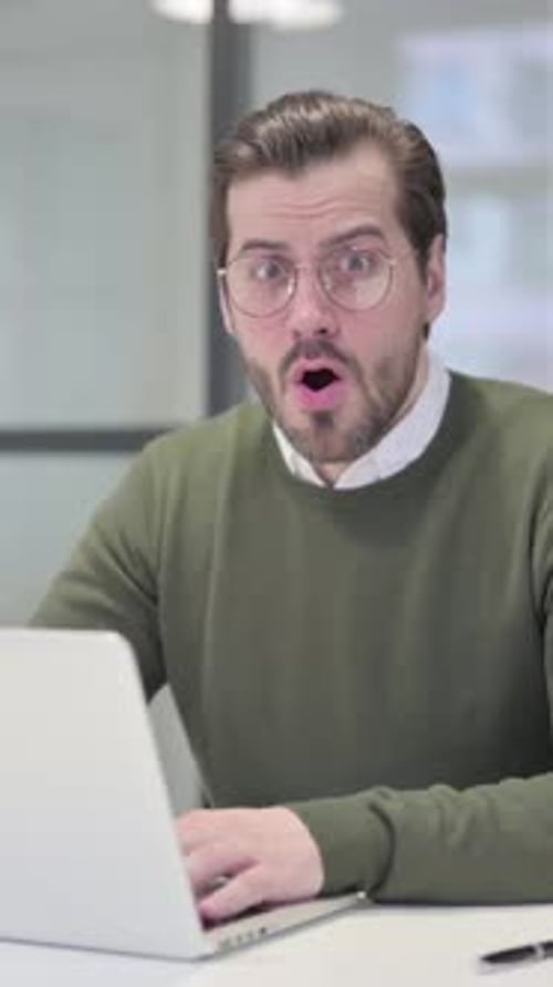 Junger Geschäftsmann fühlt sich schockiert, als er den Laptop im Büro benutzt, vertikales Video