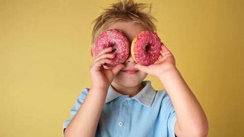 Happy Child Holding Glazed Donut Little Boy is Covering Eyes Donuts on Yellow Studio Background Kid