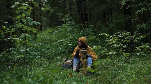 Female Hiker in Yellow Raincoat Eating Lunch Surrounded By Verdant Forest During Light Rain