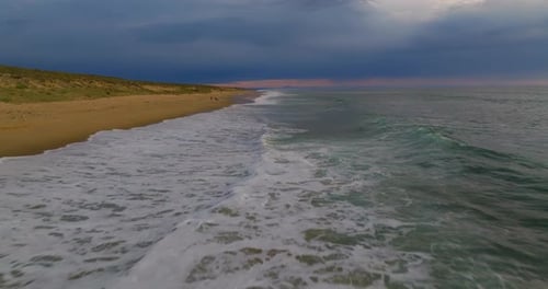 A Drone Flies Over the Ocean's Breaking Wave at Sunset