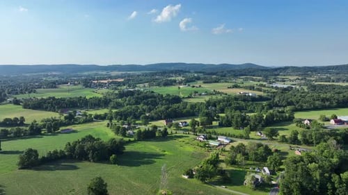 Flying over the lush green rural countryside with fields and small clusters of houses on a sunny day