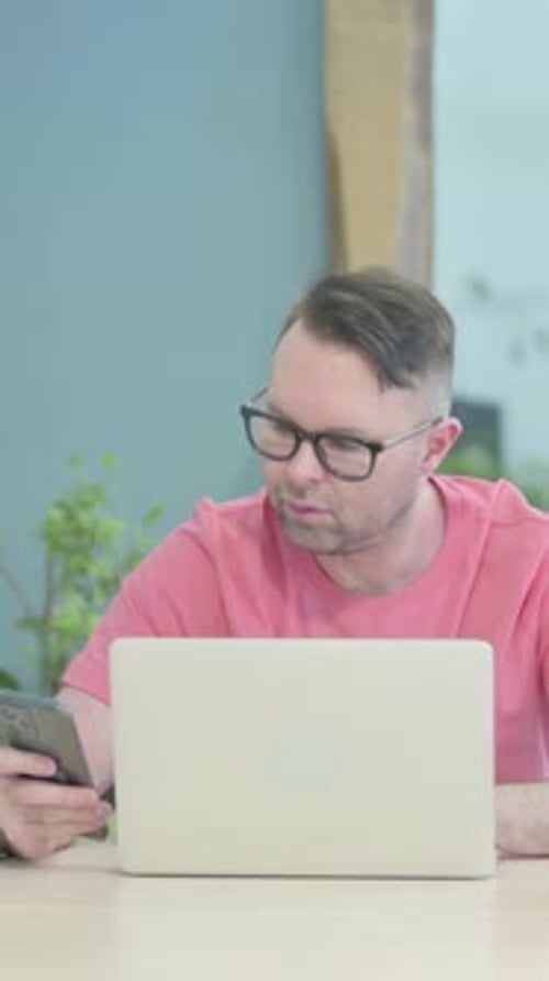 Man Using Laptop and Phone in Workplace Setting