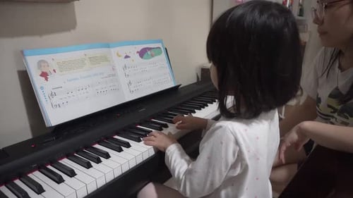Cute Girl Learning Piano with Adult Assistance