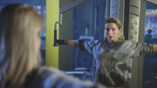 The Girl Performs Hand Exercises on the Simulator in the Gym