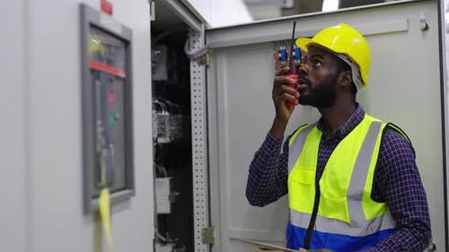 4K African man engineer working and talking on walkie-talkie at factory control room.