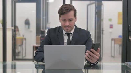 Man Working on Laptop and Cell Phone in Office