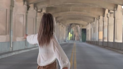 A girl spin dancing and jumping down the middle of the road under a bridge located at kansas city. P