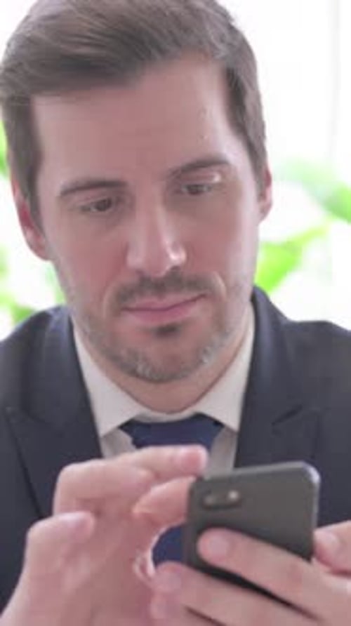 Young Businessman Browsing Internet on Smartphone in Office, vertical video