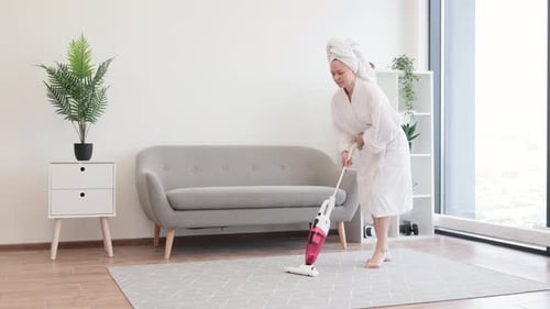 Woman vacuums rug in bathrobe indoors