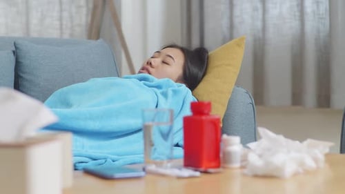 Gros plan d'une femme asiatique malade avec une couverture gelée et frissonnante allongée sur le canapé dans le salon