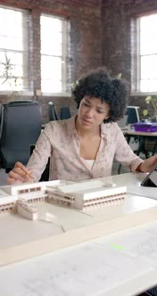 Vertical video of focused biracial casual businesswoman checking building model in slow motion