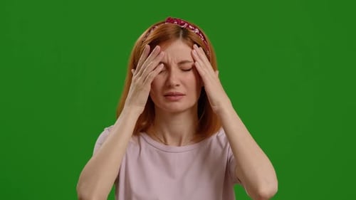 Woman with severe headache on a green screen isolated on studio background.