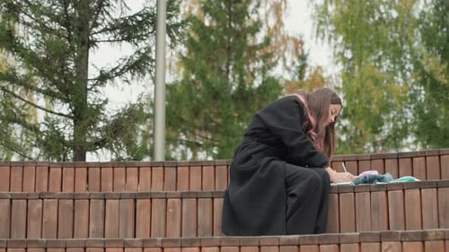 Girl Writing in Book on Wooden Outdoor Bench
