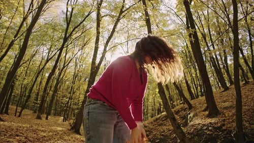 Happy Woman Throwing Orange Leaves Uphill in Autumn Park
