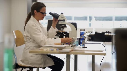 Woman in Lab Coat Uses Microscope in Laboratory