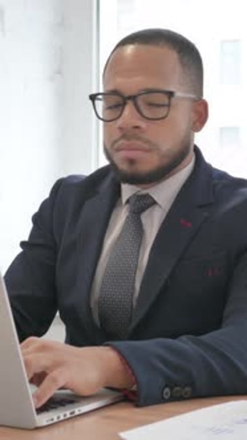 Geschäftsmann mit gemischter Rasse, der bei der Arbeit am Laptop im Büro in die Kamera lächelt, vertikales Video