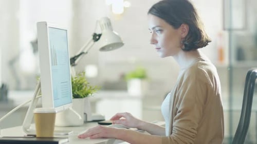Young Beautiful Woman Works at Her Desktop Computer. Sitting at Her Desk in a Light and Modern Offi