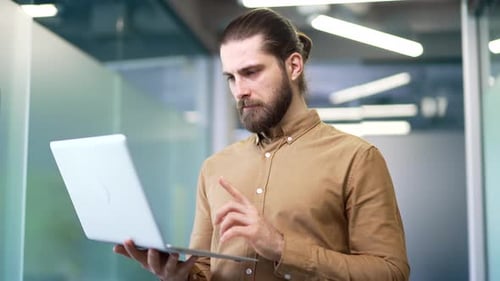 IT engineer admin works on a laptop while standing in business office of data center.