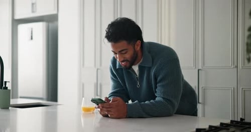 Man Using Phone in Kitchen with Orange Juice