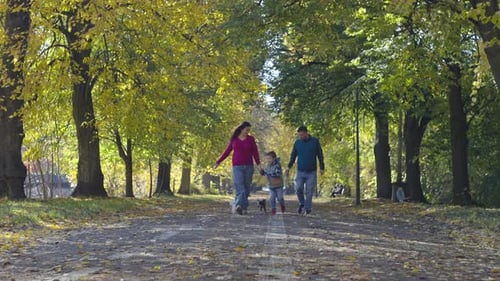Happy Family Walking on Yellow Leaves in Autumn Park