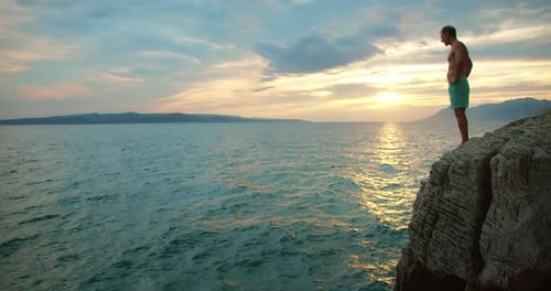 Mann taucht bei Sonnenuntergang von einer felsigen Klippe ins Meer mit malerischem Horizont und ruhigem Wasser der Adria i