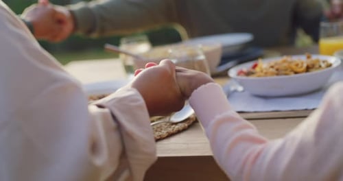 Family praying at the dinner table outside in the garden during summer at sunset