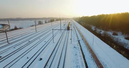 Drone flying backwards, capturing a train slowly approaching a staition during the winter, surrounde