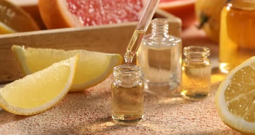 Dripping aromatic essential oil from pipette into perfume bottle among lemons at beige textured