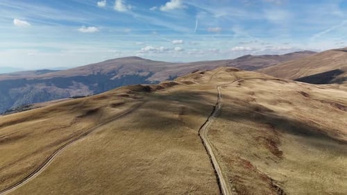 Mountain path winding through vast dry hills under a clear blue sky with distant peaks visible