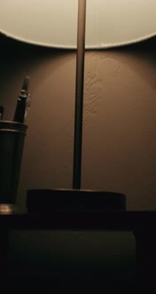 Vertical Panning Tilt Up of Flickering Lamp Creating Shadows Over Pens