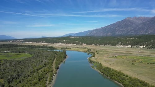 Aerial View of a Flowing River, Lush Green Trees, and Mountain Range Under a Blue Sky